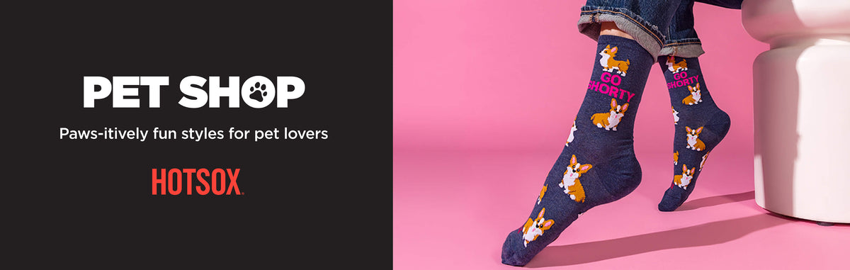 A person wearing dark navy socks with a cartoon dog pattern and the word 'HOTSOX' in pink, standing against a bright pink background. The left side of the image has a black panel with the text 'PET SHOP', 'Paws-itively fun styles for pet lovers', and the brand name 'HOTSOX' in orange.