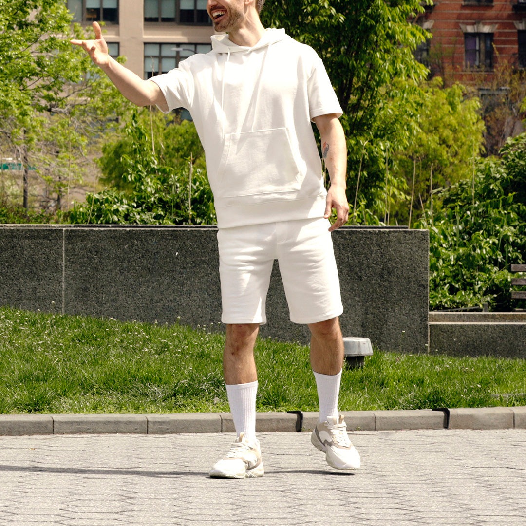 Person wearing a white outfit standing outdoors with greenery in the background