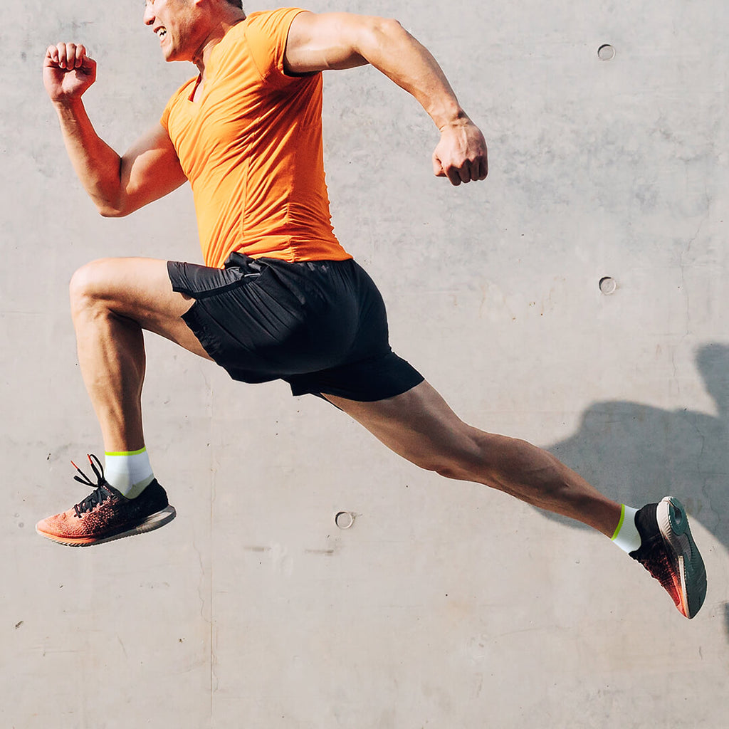 Man in orange shirt and black shorts running in front of a concrete surface