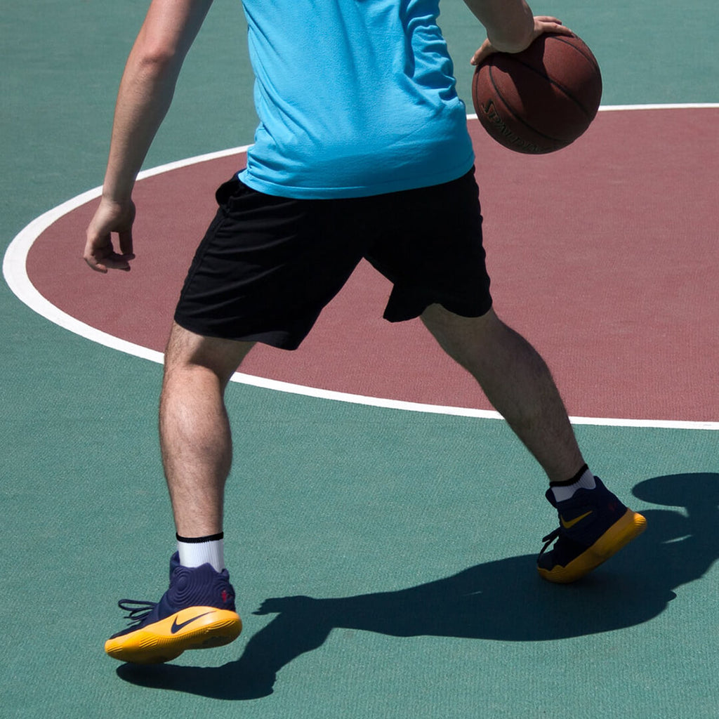 Person holding a basketball on a court wearing a blue shirt, black shorts, and colorful shoes.
