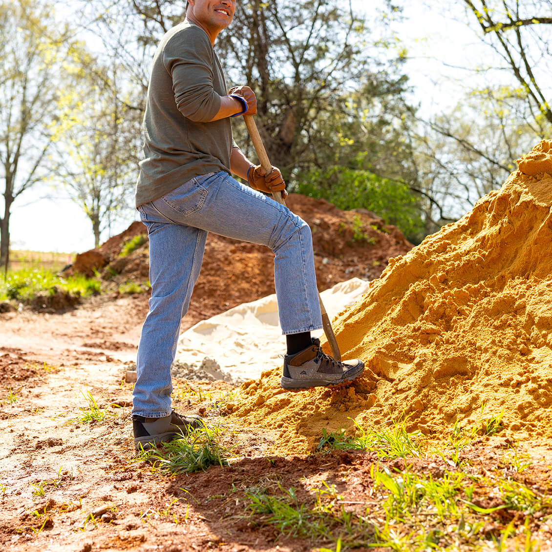 Man digging in a pile of sand with a shovel outdoors