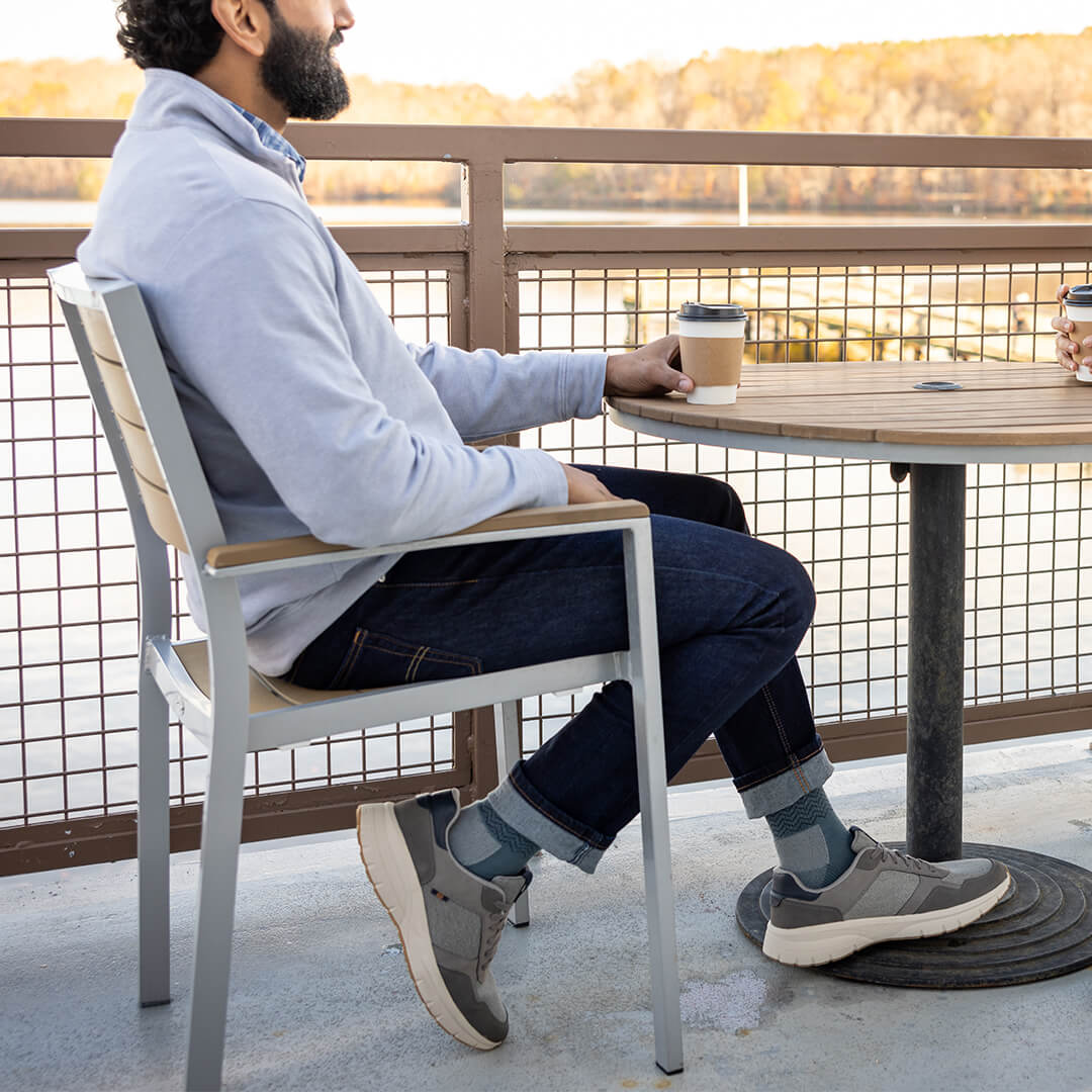 Man sitting at a table on a balcony with a view of trees and water.
