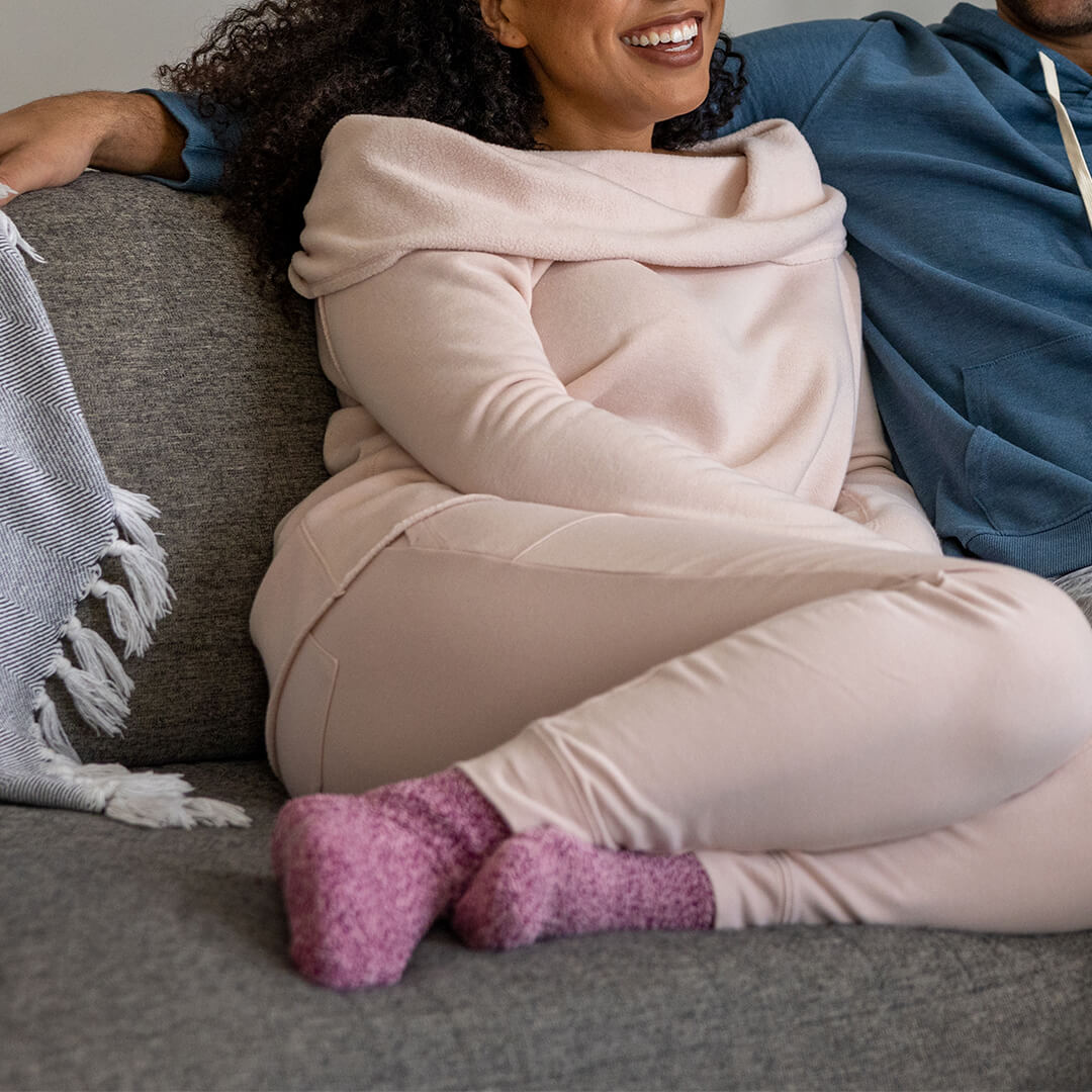 Person wearing a pink outfit with purple socks sitting on a couch.