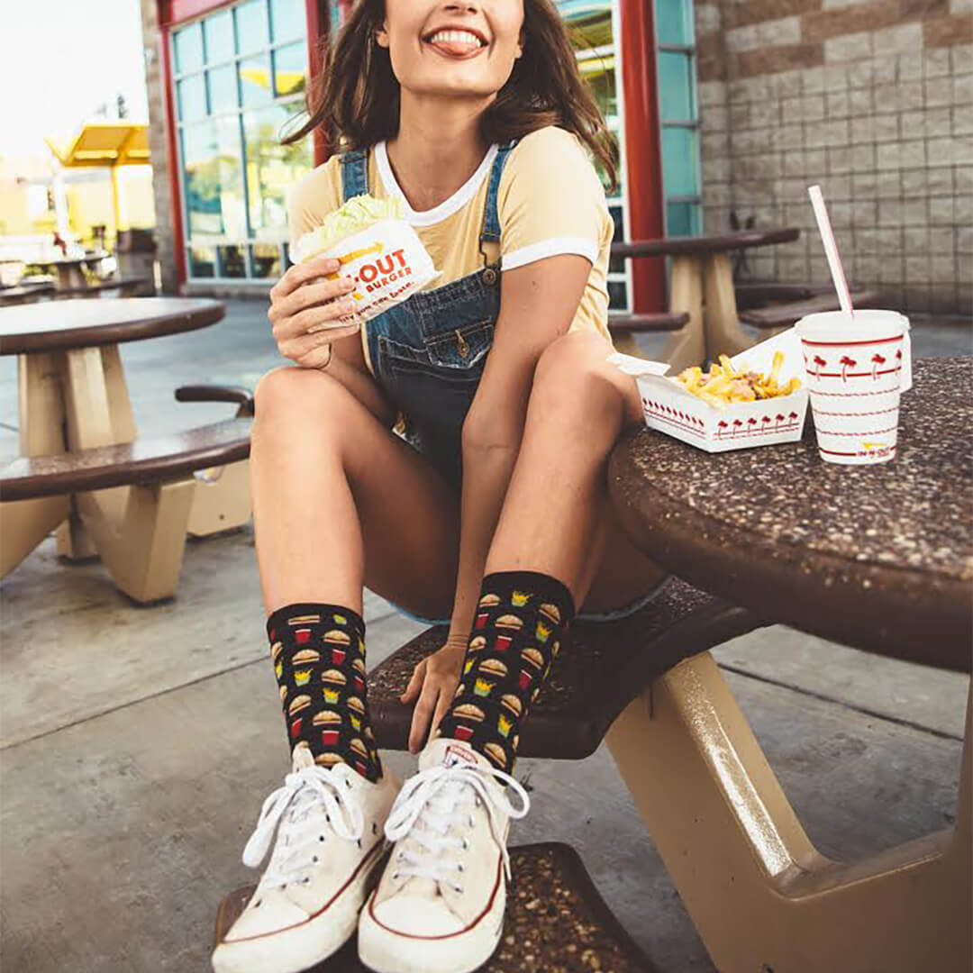 Person sitting at an outdoor dining table with fast food, wearing hamburger-patterned socks.