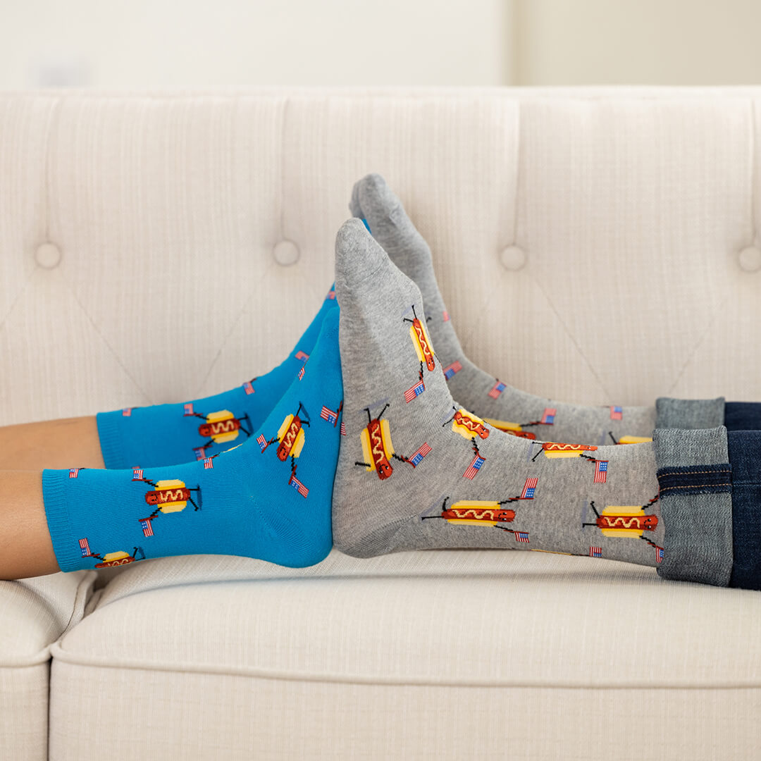 Two pairs of socks, one blue and one gray, with hot dog pattern on a light-colored couch.