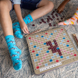 Children playing Scrabble on a carpeted floor with one child wearing shark-patterned socks. thumbnail