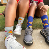 Two pairs of feet wearing colorful taco socks and sneakers on a grassy background thumbnail