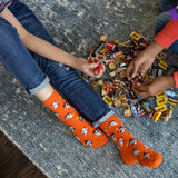 Kids wearing orange socks with Halloween patterns, sitting on a carpeted floor with candy bars. thumbnail