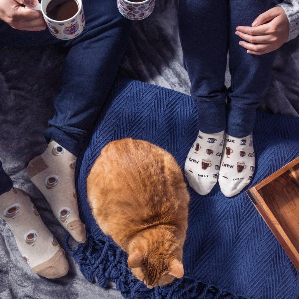 Two people sitting on a couch with a cat, wearing socks with coffee cup designs.