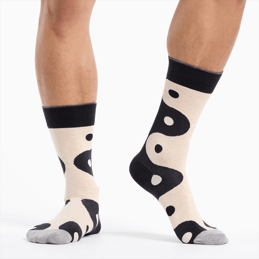 Black socks with a black and white yin yang pattern worn by a person on a white background
