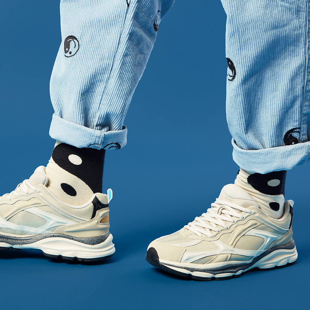 Person wearing light blue jeans and black and white yin yang socks against a blue background