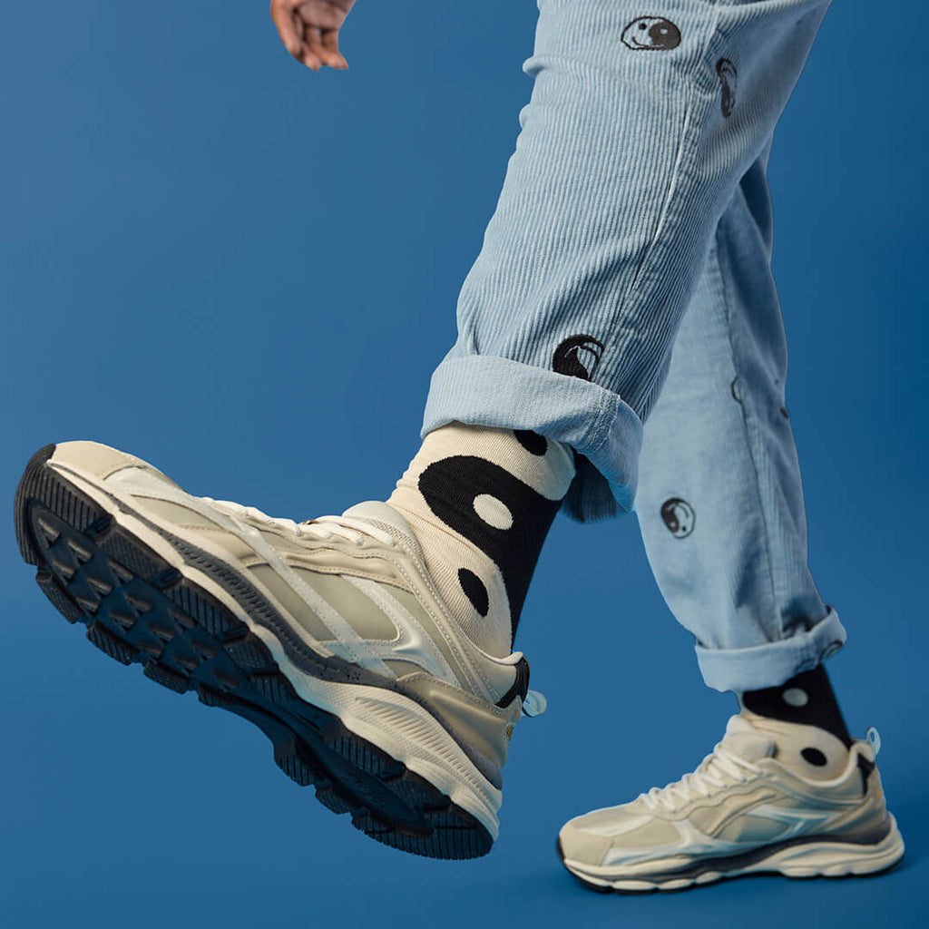 Person wearing beige sneakers, light blue jeans and black and white yin yang socks against a blue background