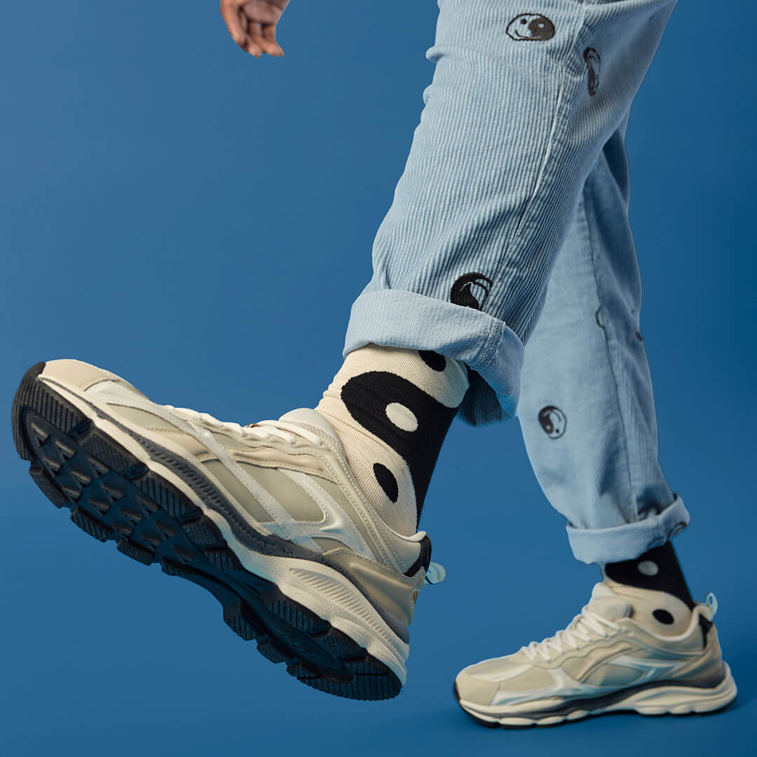 Person wearing beige sneakers, light blue jeans and black and white yin yang socks against a blue background