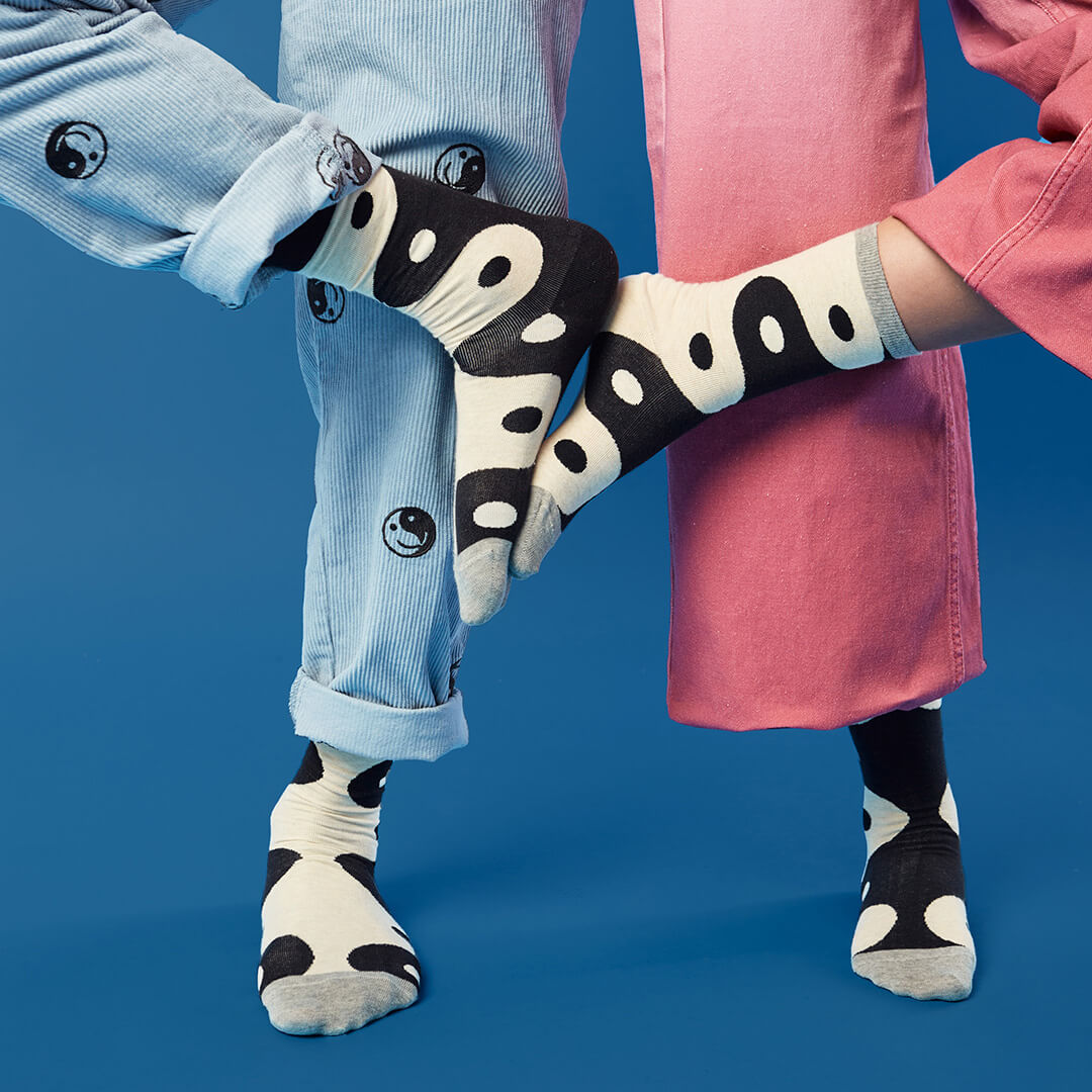 Two pairs of legs wearing black and white yin yang socks against a blue background.