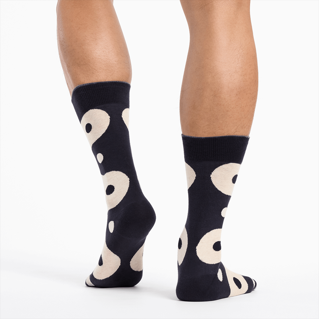Black socks with a black and white yin yang pattern worn by a person on a white background