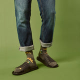 Person wearing blue jeans, sandals, and patterned beer and pizza slice socks on a green background thumbnail