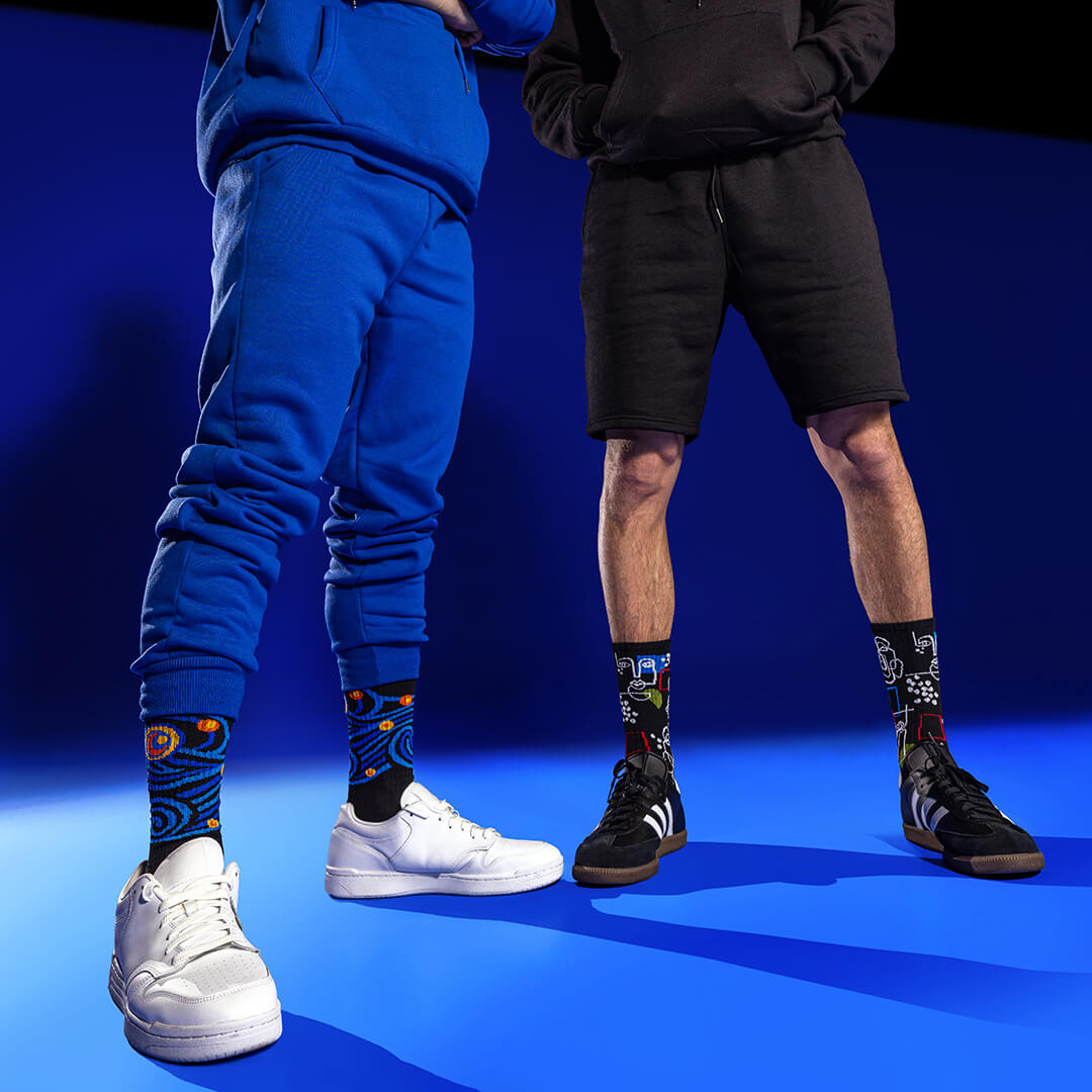 Two people wearing colorful socks with famous painting designs on a blue background