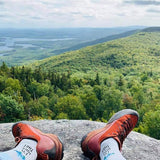 Red hiking boots on a rock with a scenic view of green hills and lakes.