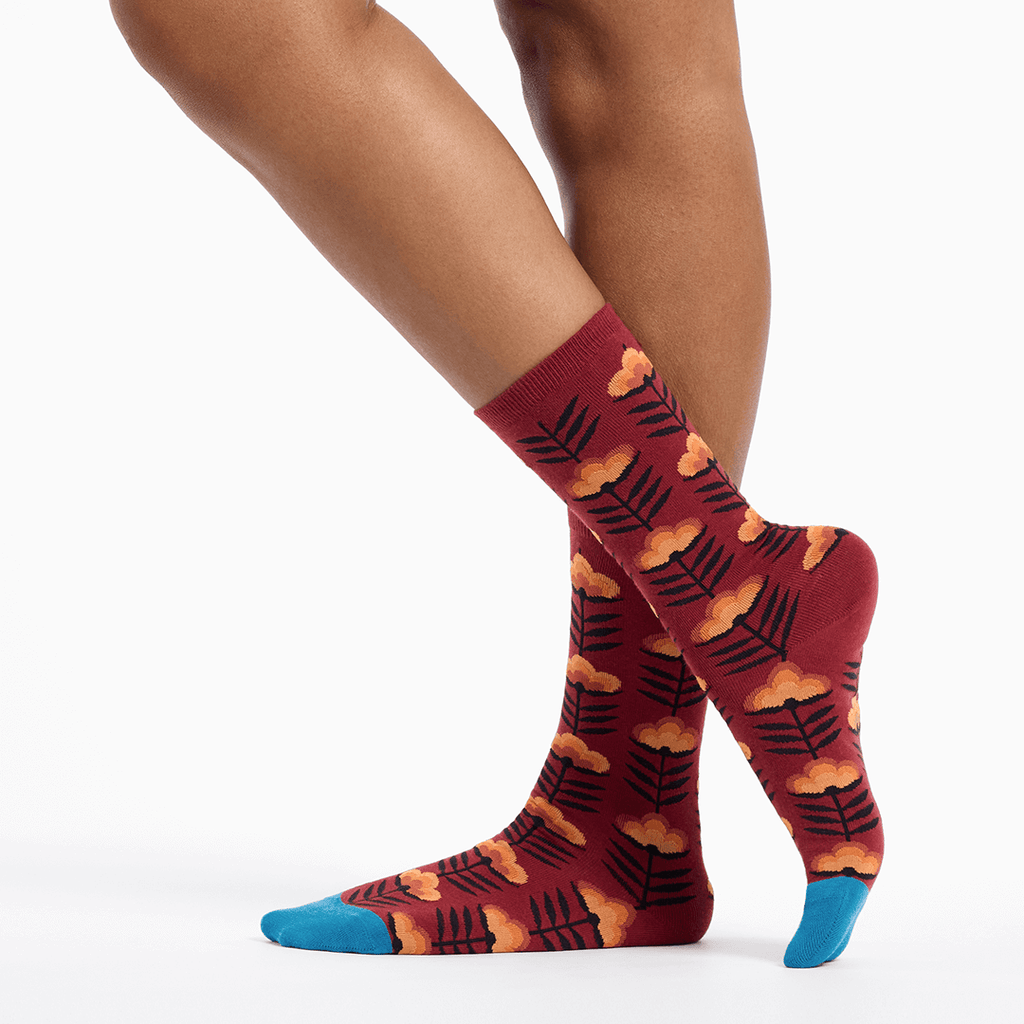 Red socks with a floral leaf pattern worn by a person on a white background