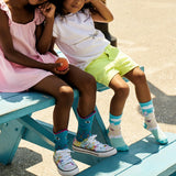 Two children sitting on a blue bench wearing colorful socks. thumbnail
