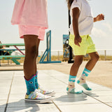 Two children wearing colorful socks and shoes on a sunny day. thumbnail