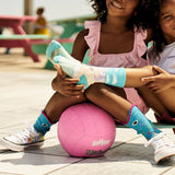Two children sitting on a pink ball wearing colorful socks with a beach background