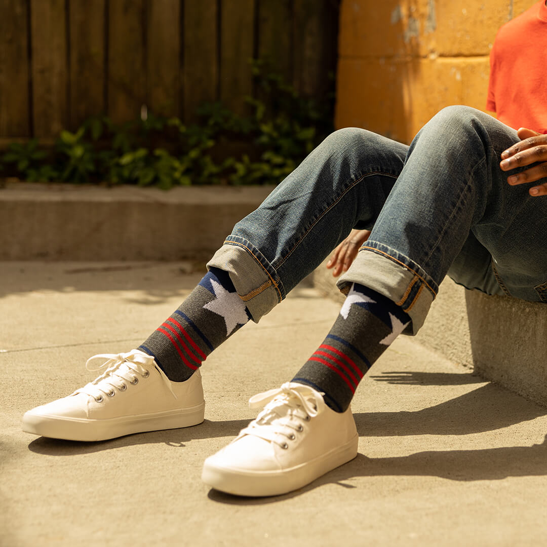 Person wearing white sneakers and patterned socks sitting on a concrete surface.