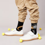 Person wearing black socks with graphic designs, beige pants, and white sneakers on a light gray background. thumbnail
