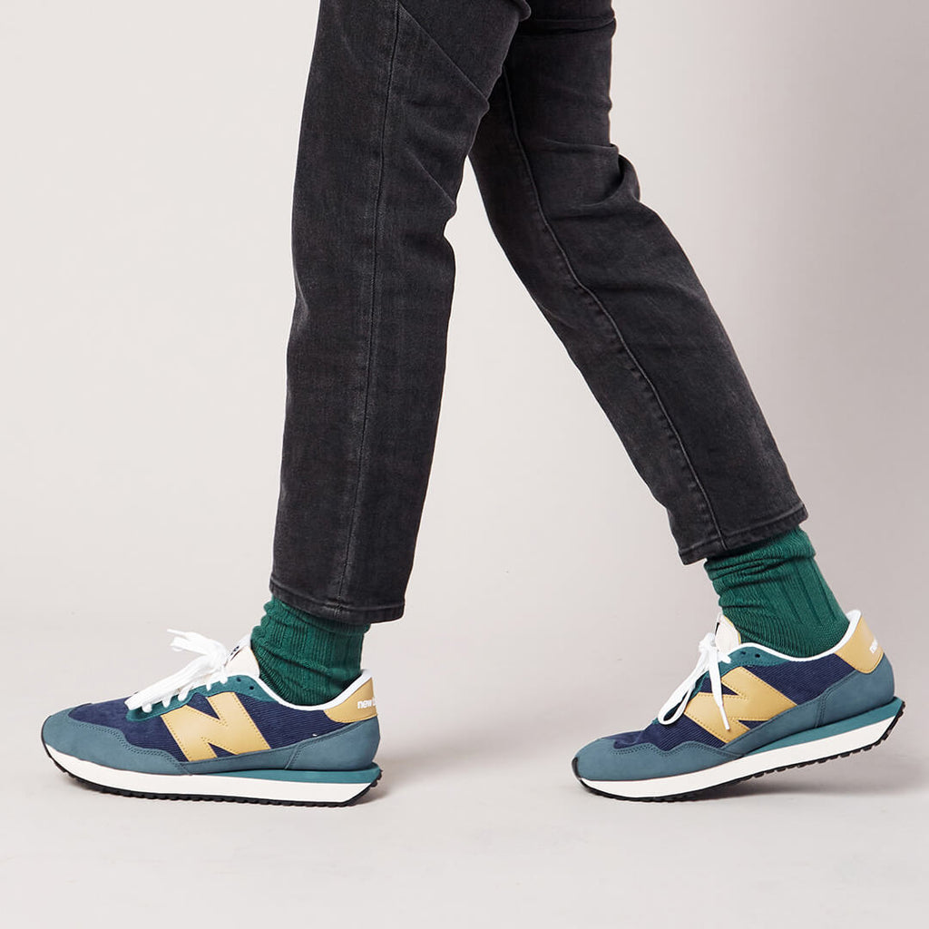 Person wearing blue and yellow sneakers with green socks on a plain background