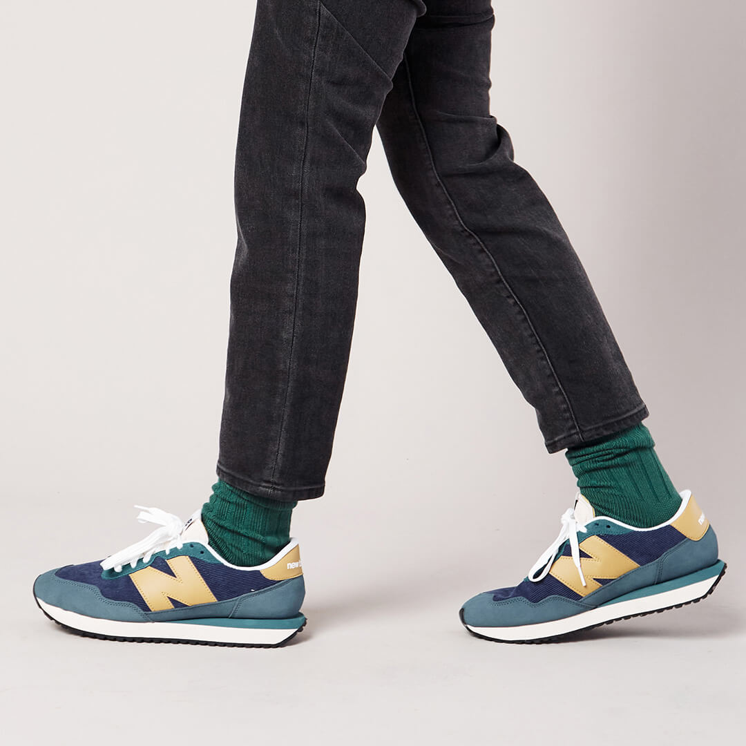Person wearing blue and yellow sneakers with green socks on a plain background