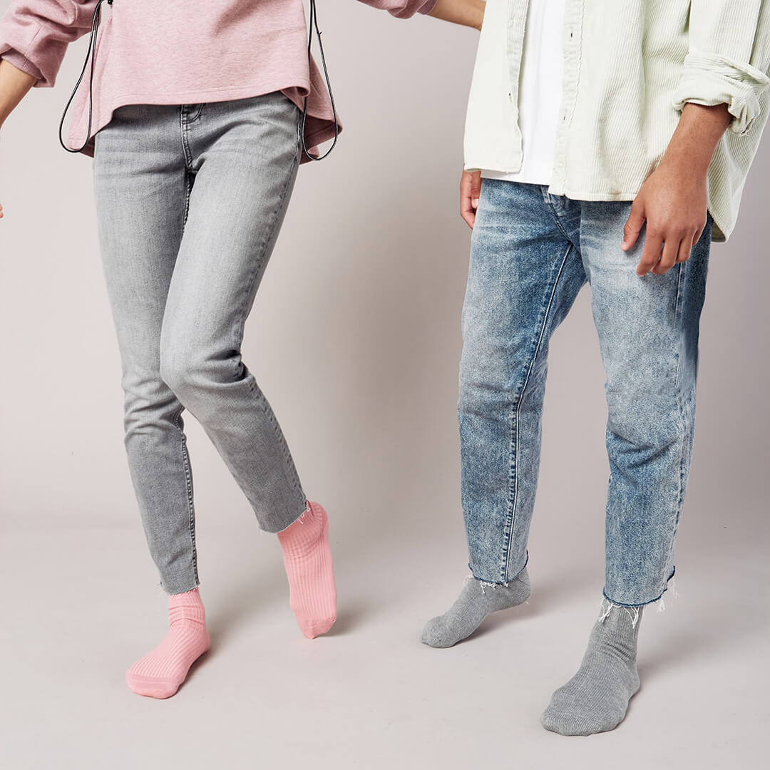 Two people wearing jeans and socks on a plain background
