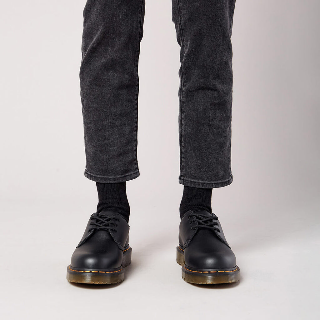 Person wearing black leather shoes and gray jeans on a plain background