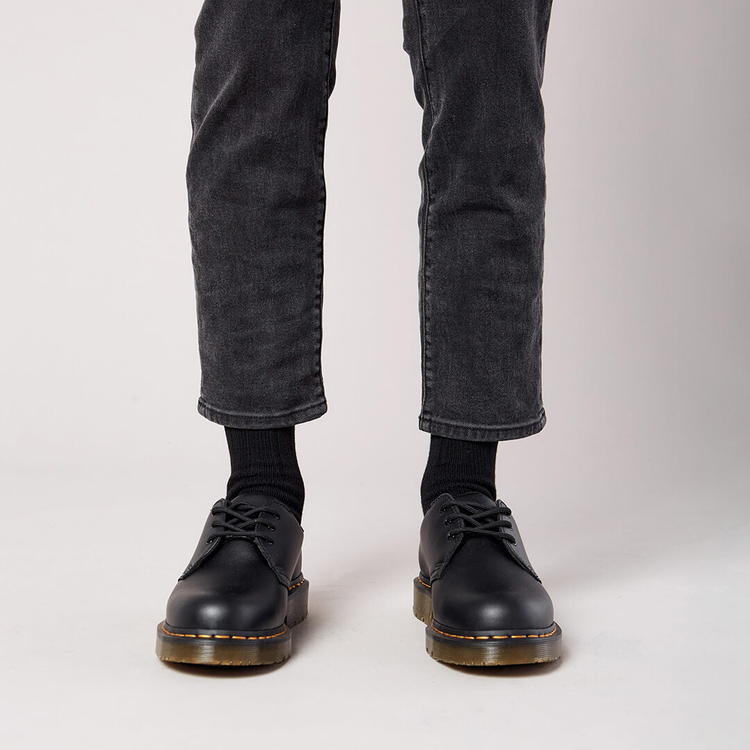 Person wearing black leather shoes and gray jeans on a plain background