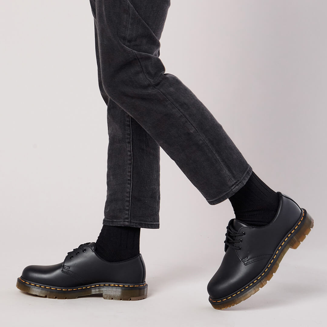 Person wearing black leather shoes with brown soles on a light gray background
