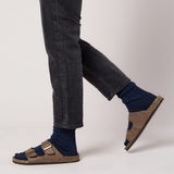 Brown sandals worn with dark jeans and navy socks on a light gray background thumbnail