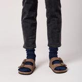Person wearing blue socks, dark jeans, and brown sandals on a white background thumbnail