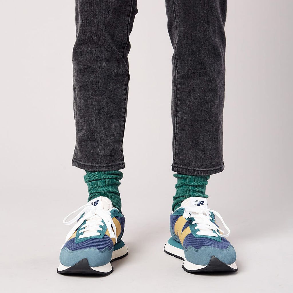Person wearing green socks, black jeans, and colorful sneakers on a plain background