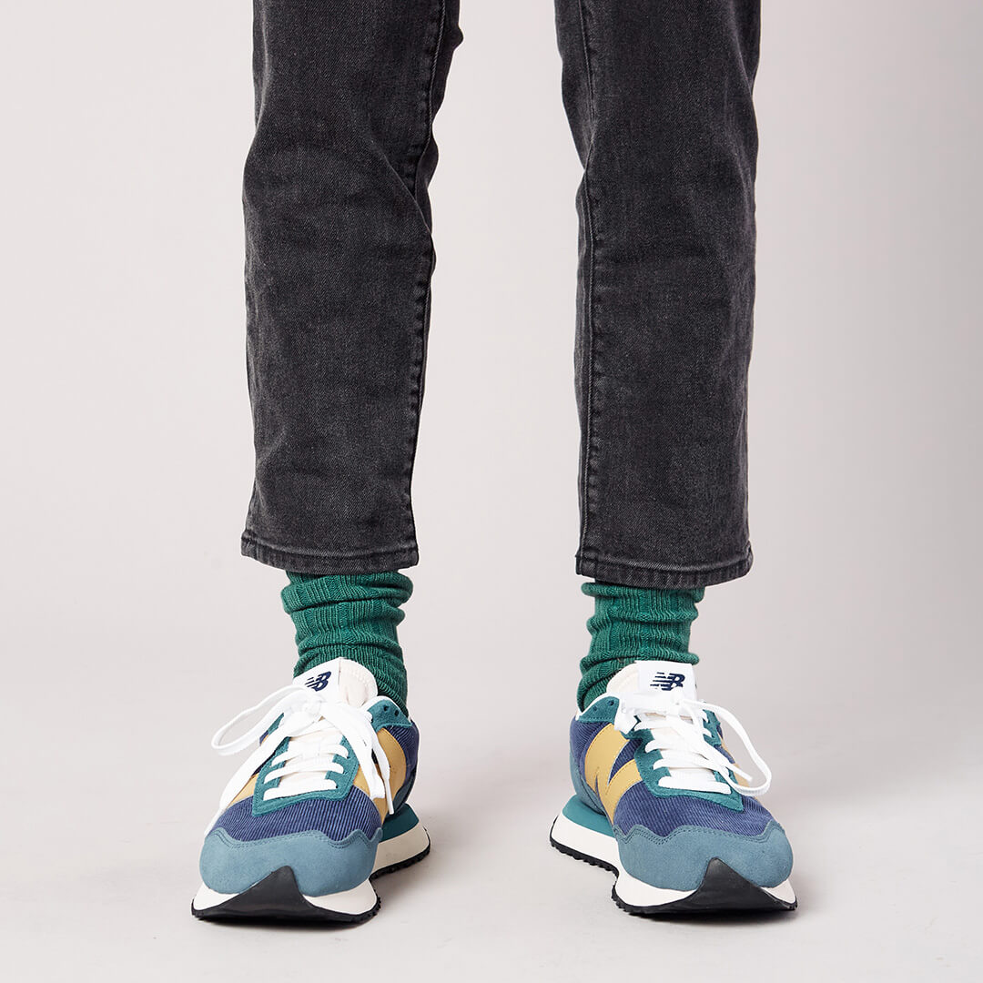 Person wearing green socks, black jeans, and colorful sneakers on a plain background