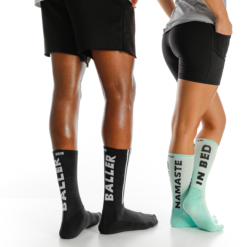Two pairs of socks with text on them worn by people, one black with 'BALLER' and one green with 'NAMASTE IN BED'.