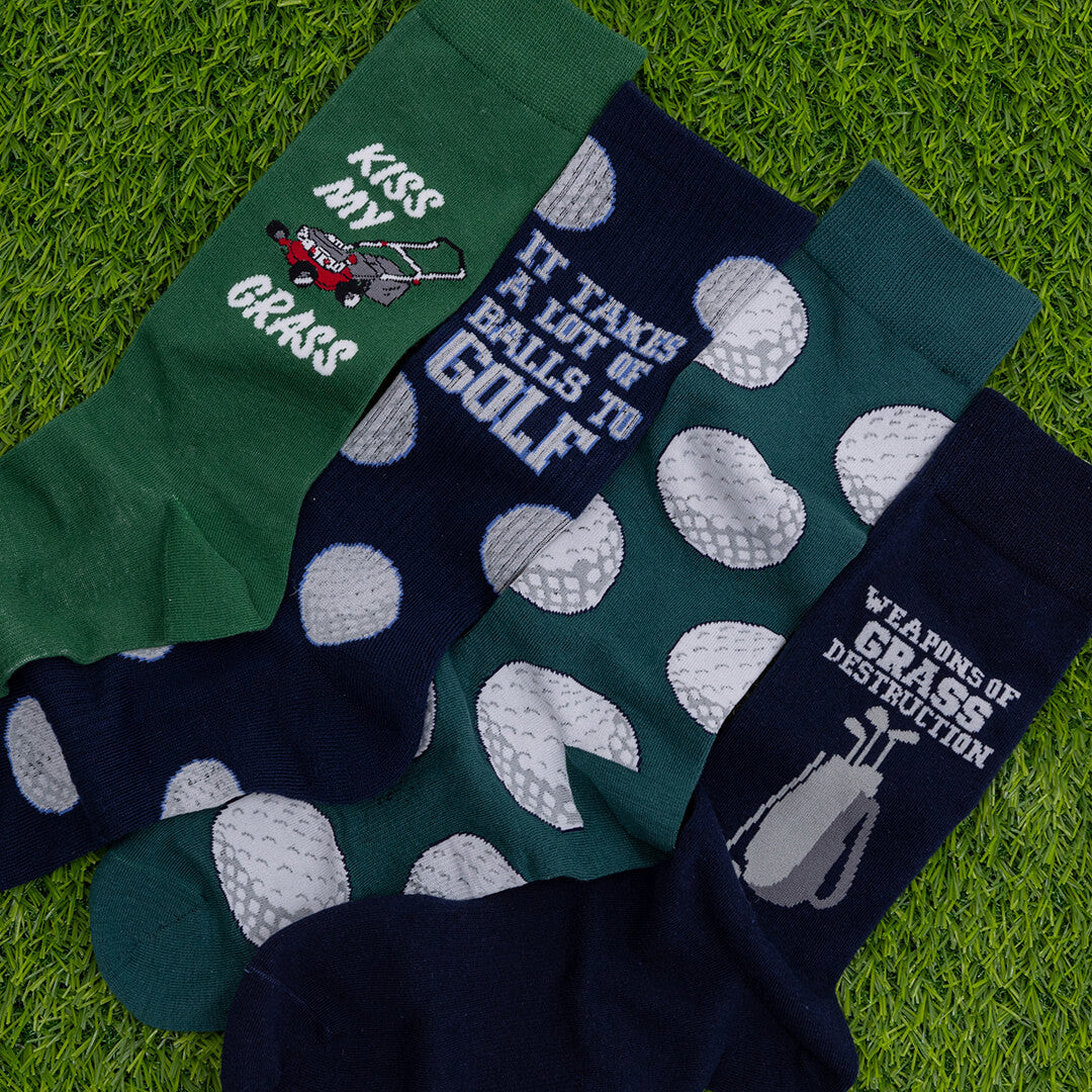 Four pairs of socks with humorous golf-themed designs on a grass background