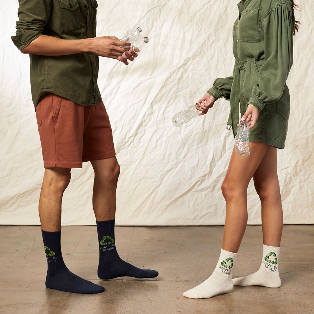 Two people wearing socks with recycling symbols, one in navy and the other in white, against a neutral background.