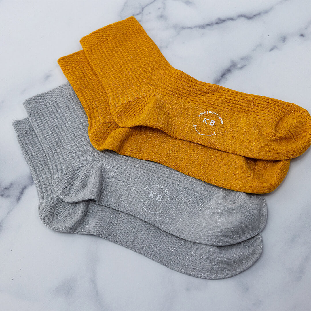 Two pairs of metallic socks, one gold and one silver, on a marble surface.