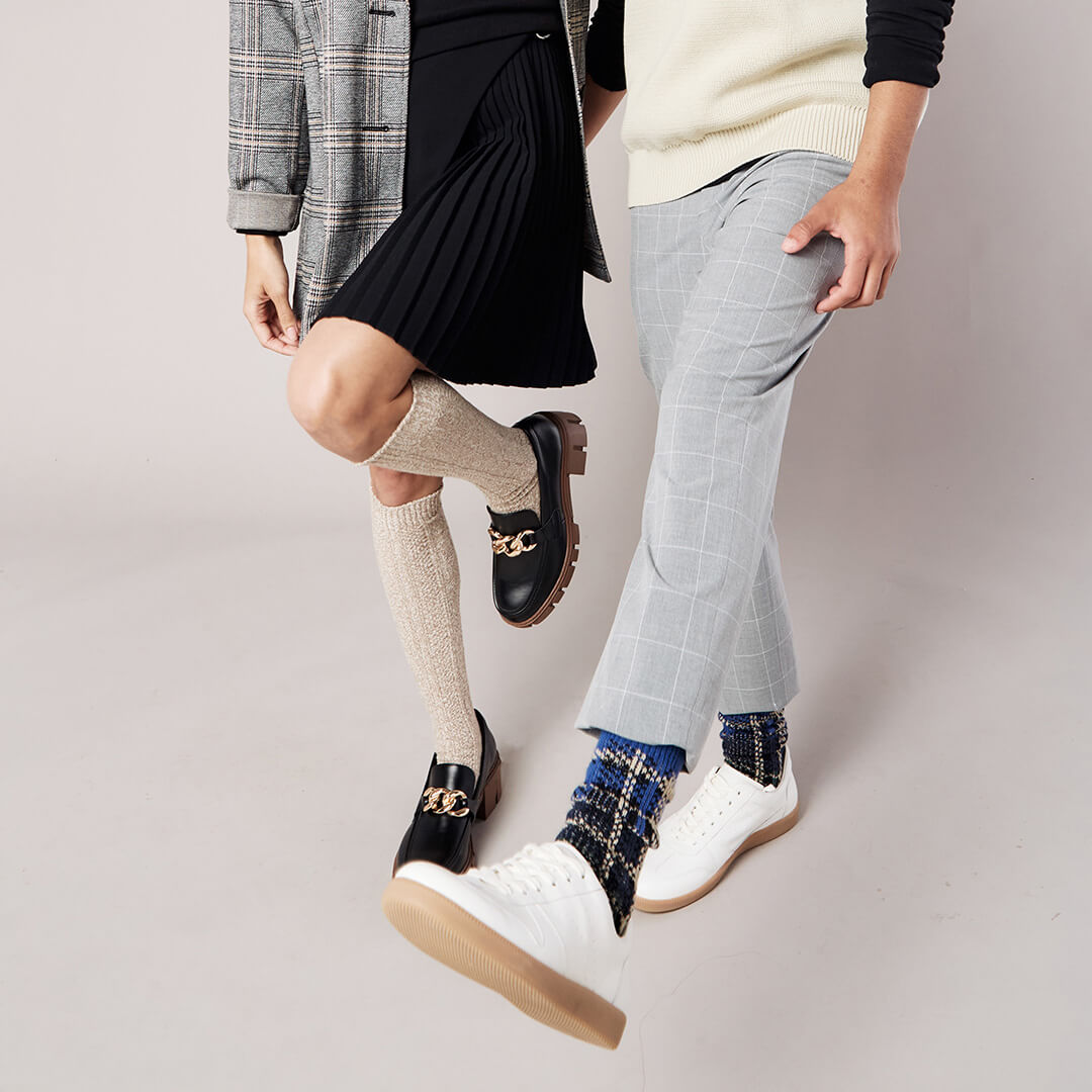 Two people wearing different styles of socks with a neutral background