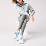 Person wearing a light gray tracksuit with blue jersey slippers on a white background thumbnail