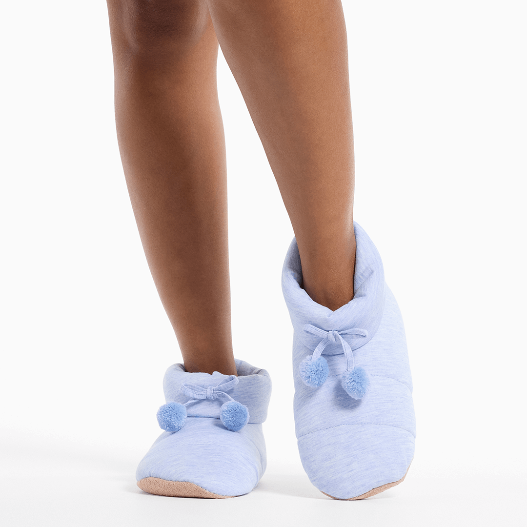 Light blue slippers with pom-poms worn by a person on a white background