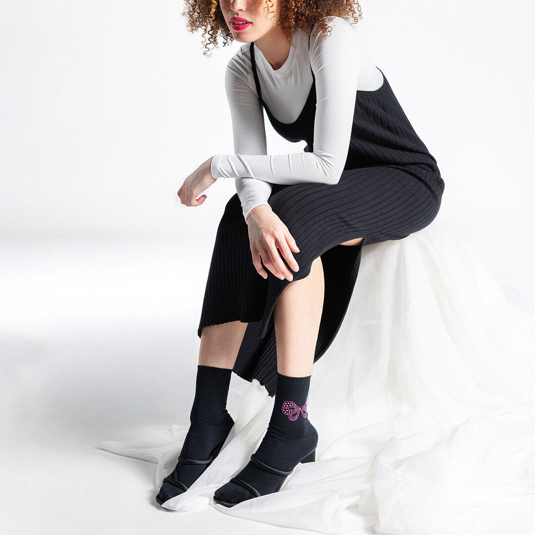 Woman wearing black socks with a pink rhinestone bow on a white background.