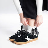 Black sneakers with white socks and a bow embellishment on a white background thumbnail