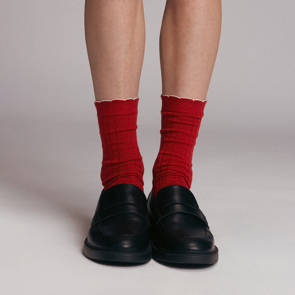 Red socks with white cuffs worn with black shoes on a neutral background
