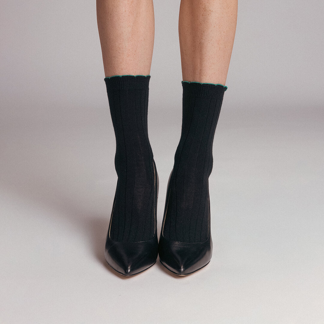 Black high-heeled shoes worn with black socks on a neutral background