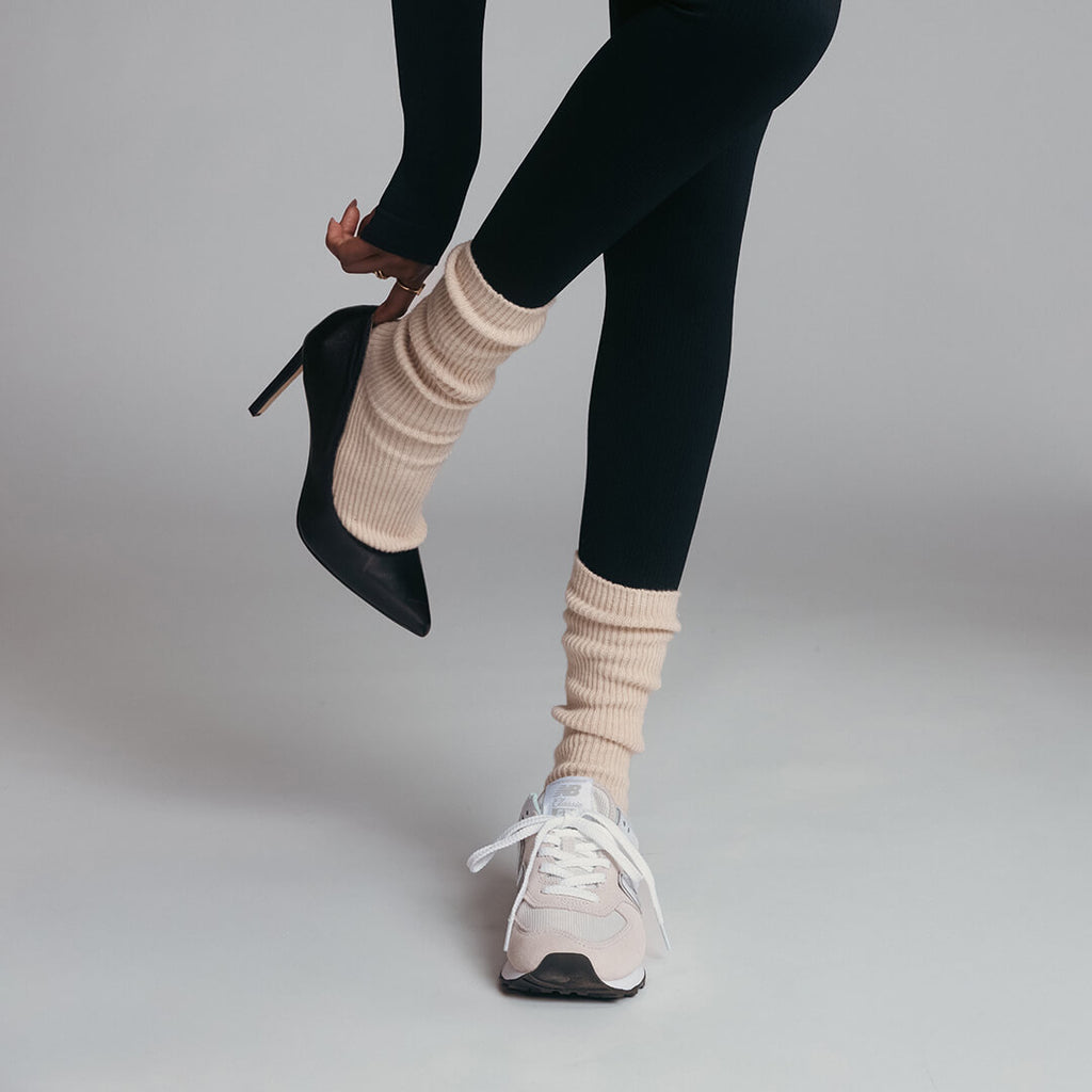 Person wearing black high heels and white sneakers with beige socks on a plain background